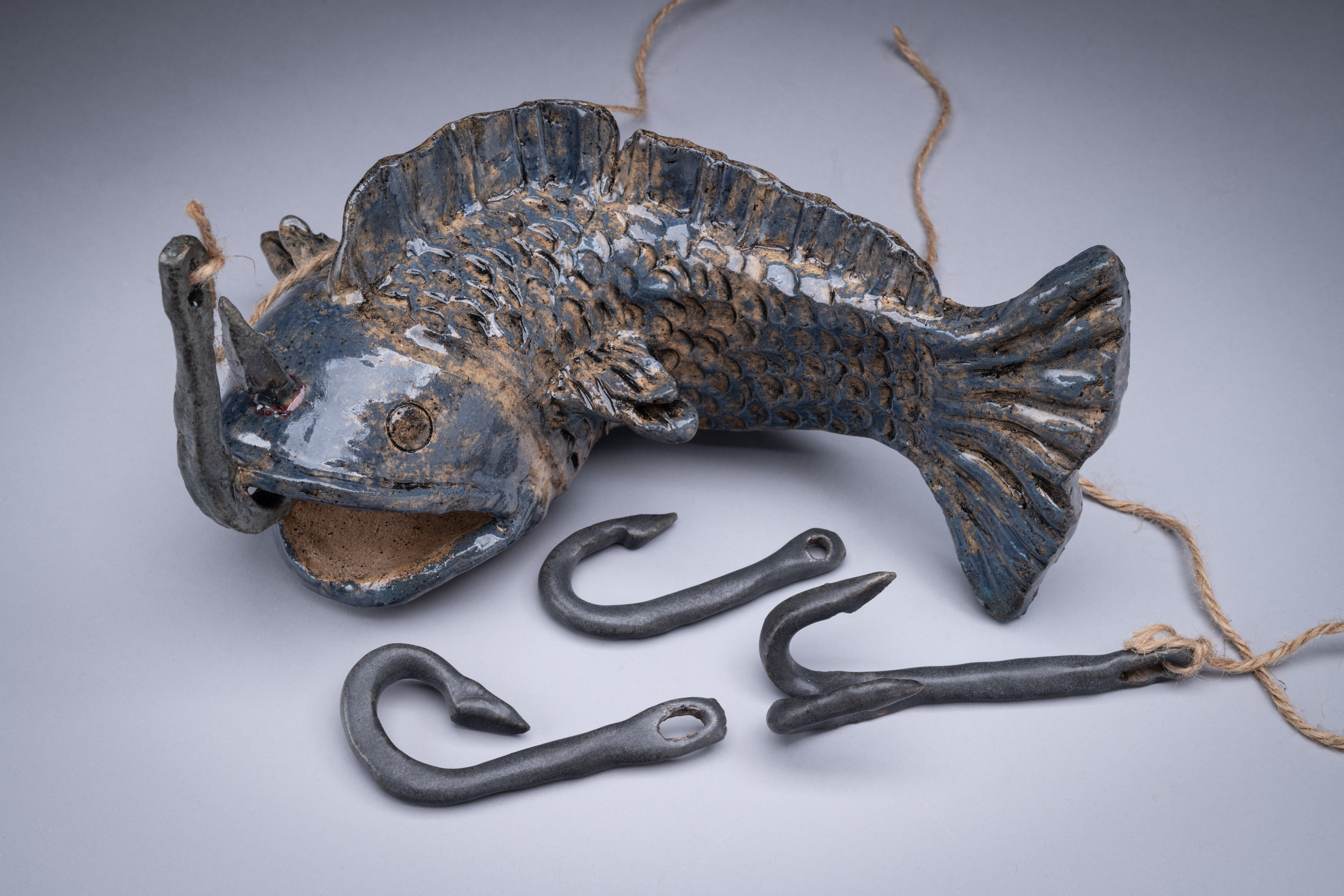 A glazed ceramic fish surrounded by hand-built hooks on twine